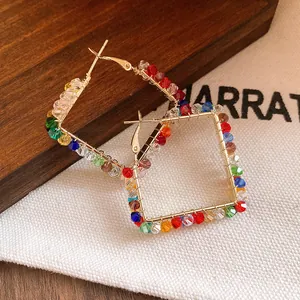 Macro view of colorful faceted glass beads hand-wrapped on gold-tone square hoop earrings.