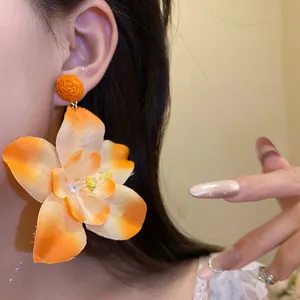 Macro close-up view of vibrant orange fabric flower earring with a raffia stud detail