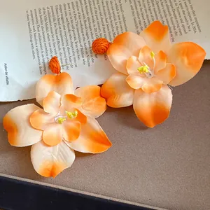 Detailed view of oversized orange fabric flower earrings with raffia accents for beach vacation.