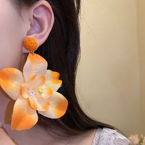 Detail view of vibrant orange fabric flower earrings featuring a woven raffia ball top