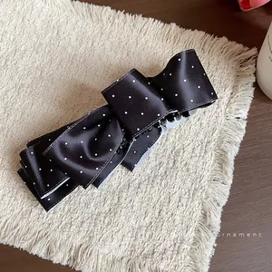 Elegant black and white polka dot bow hair clip on a textured beige fringed mat