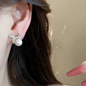 Primer plano detallado de elegantes pendientes de botón con lazo y perla usados en la oreja