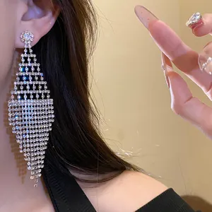 Detailed macro shot of exaggerated rhombic rhinestone tassel earrings on ear.