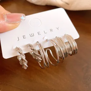 Close-up detail of a set of diverse silver geometric hoop earrings on white jewelry card