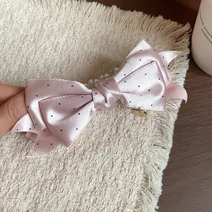 Close-up view of a pink satin polka dot bow hair clip with an elegant golden charm