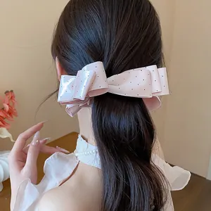 Close-up of an elegant pink polka dot bow hair clip styled on a woman's dark ponytail
