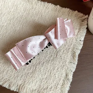 Detailed view of the pink satin polka dot bow hair clip on a textured background.