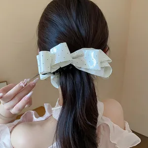 Detailed macro view of an elegant white polka dot bow hair clip styled on dark hair