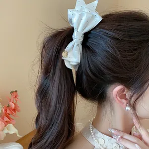 Detailed view of an elegant white polka dot bow hair clip on a model's ponytail