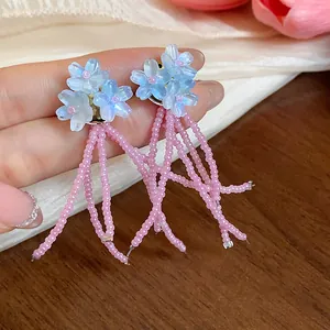 Primo piano di orecchini a lobo con fiori blu e lunghe nappe di graziose perline rosa