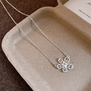 Detail of a delicate silver necklace with a hollowed-out flower pendant and zircon.