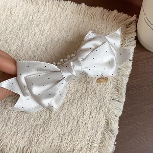 Close-up detail of a white polka dot bow hair clip featuring an elegant gold charm detail