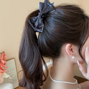 Detailed view of an elegant black polka dot fabric bow hair clip on a ponytail