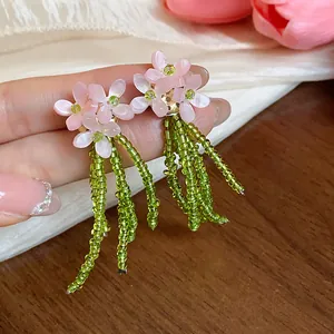 Dettaglio degli orecchini a lobo rosa a forma di fiore con delicate nappe di perline.