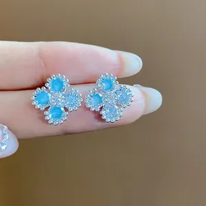 Dettaglio macro di orecchini a lobo a fiore con pietre blu e zirconi cubici trasparenti.