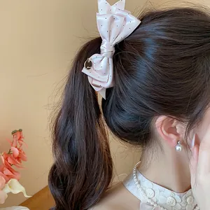 Close-up detail shot of a pink polka dot bow hair clip worn on a brown ponytail.