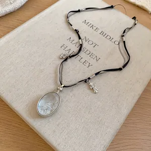 Gros plan d'un collier croix argenté avec pendentif ovale en pierre de style ins.