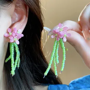 Primo piano di orecchini a fiore in vetro con petali rosa e nappe di perline verdi