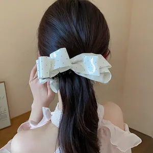 Close-up detail of a stylish white polka dot bow hair clip worn on a ponytail back view.