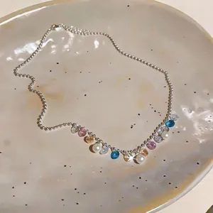Dettaglio di una collana di perle scintillanti con gocce di gemme colorate su un piatto.