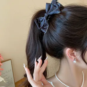 Elegant black polka dot bow hair clip made of satin fabric shown in a detail view.