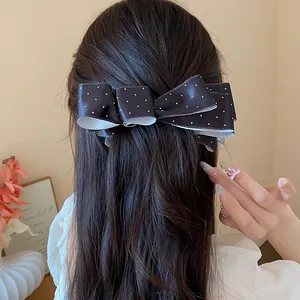 Detail view of an elegant black polka dot bow hair clip worn in dark hair