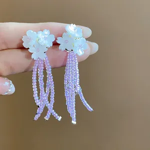 Primo piano di orecchini a fiore bianco con nappe di perline viola e ago d'argento.