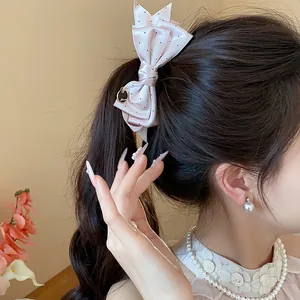 Close-up detail of a pink polka dot satin bow hair clip worn on a model ponytail