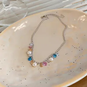 Dettaglio di una collana d'argento con pietre preziose colorate e perle bianche.