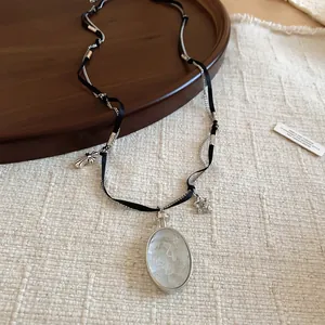 Vue détaillée du collier avec ruban noir et chaîne argentée avec le pendentif ovale