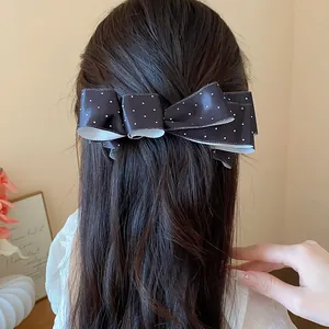 Detailed macro view of a large black and white polka dot ribbon bow hair clip on hair.