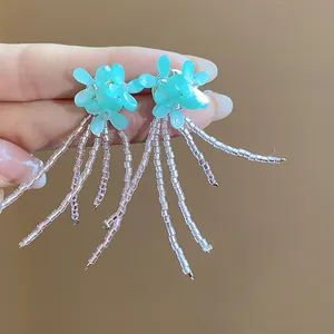 Dettaglio di orecchini a fiore azzurro con lunghe nappe di perline iridescenti