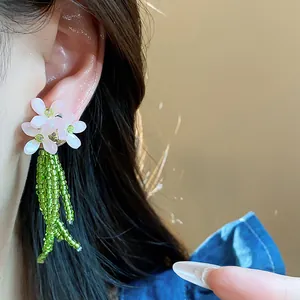 Dettaglio orecchini a fiore rosa con nappine in perle di vetro verde e perni in argento.