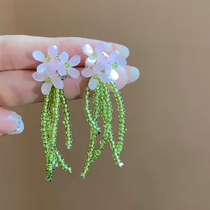 Primo piano di orecchini a fiore rosa con lunghe nappe di perline di vetro verdi.