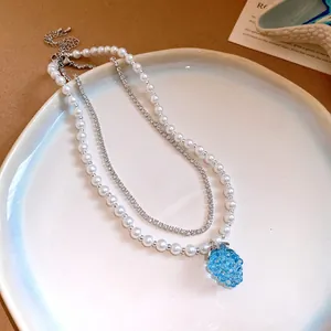 Detailed view of a layered necklace with white pearls and a blue resin grape pendant.