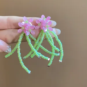 Dettaglio degli orecchini a fiore rosa in vetro con lunghe nappe di perline verdi.