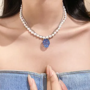 Detail of resin grape pendant on layered pearl and rhinestone necklace worn by model