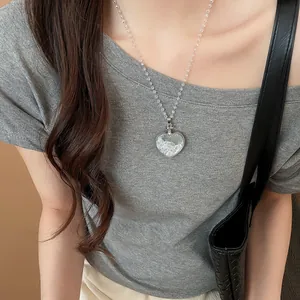 Détail d'un collier pendentif en cristal en forme de cœur porté par un mannequin en gris