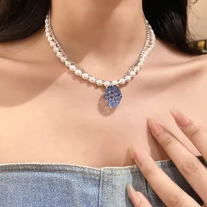 Close-up of a double-layer pearl and rhinestone necklace with a blue resin grape pendant.