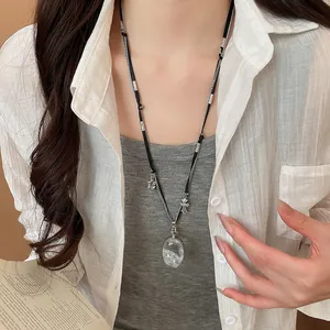 Détail d'un collier long avec pendentif en cristal ovale et breloque croix en argent.