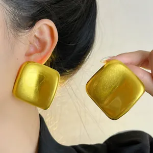 Détail montrant la texture métallique et la taille de boucles d'oreilles carrées dorées
