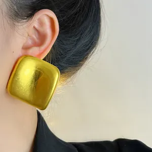 Gros plan de grandes boucles d'oreilles carrées dorées avec une finition mate chic