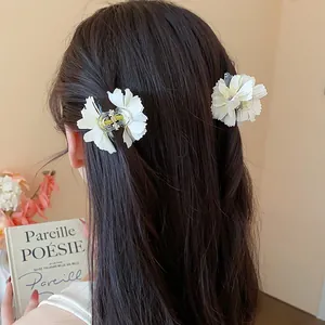 Eleganti fermagli per capelli a forma di fiore bianco crema su lunghi capelli scuri e mossi