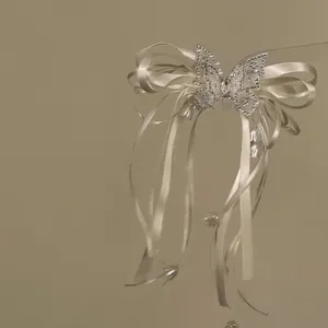 Close-up detail of a cream satin bow hair clip with rhinestone butterfly and tassels