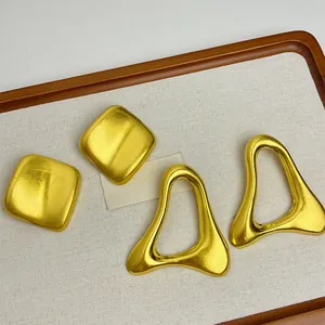 Détail de boucles d'oreilles géométriques dorées aux formes carrées et triangulaires.