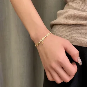 Detail of a gold-plated bow and star charm bracelet worn on a female wrist.