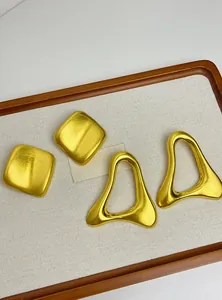 Détail de boucles d'oreilles clous géométriques dorées sur un plateau de présentation épuré