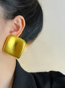 Gros plan d'une grande boucle d'oreille carrée dorée géométrique portée sur une oreille