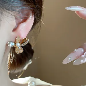 Close-up detail showing a flower-shaped earring with amber crystals and a pearl on model.