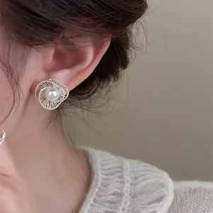 Detail view of elegant silver hollow swirl pearl stud earrings worn by a model